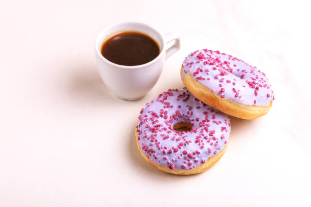 istock Two delicious lilac donuts with sprinkle and cup of coffee on light marble background 1080621638