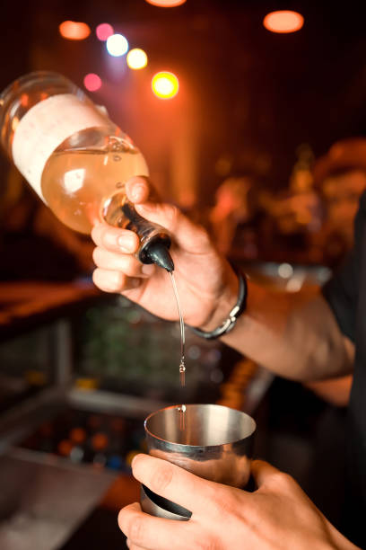 Male bartender is making cocktail pouring alcohol from shaker to glass at bar background. Barman at work.