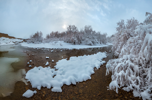 Winter river on a sunny day. Snowy banks of the river. Forest, trees in flakes of snow.