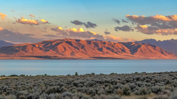 Utah lake and red mountain under dramatic sky Utah lake and red mountain under dramatic sky. The calm blue Utah Lake against a striking mountain with a red glow at sunset. Beautiful scenery of a lake with a boundless cloudy sky overhead. lake utah stock pictures, royalty-free photos & images