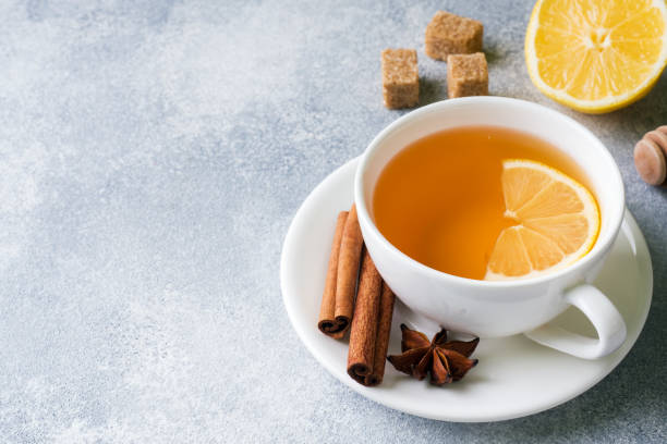Cup of tea with lemon and brown sugar, cinnamon and anise on the table.