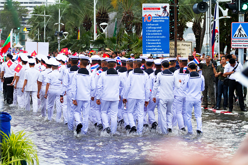Many asean navy soldiers walking in flooded Beach Road in Pattaya during Asean fleet parade. Rearshot of soldiers. Along street tourists and photographers are standing.