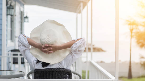 stile di vita da ragazza che indossa il cappello estivo nella giornata di sole rilassandosi prendendolo facilmente seduto felicemente sotto il portico sulla spiaggia sul lungomare godendo di una sana qualità della vita per il concetto di vacanza - casa al mare foto e immagini stock