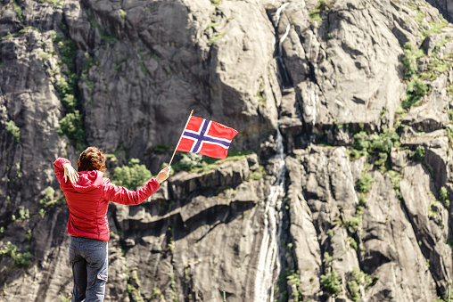 Tourist woman with norwegian flag in rocky stone mountains.