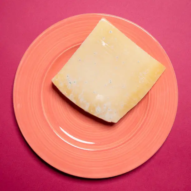 A piece of blue cheese on a pink plate. Still life, top view.