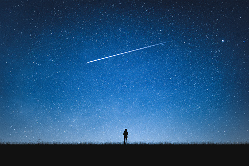 Silhouette of girl standing on mountain and night sky with shooting star. Alone concept.