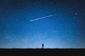 Silhouette of girl standing on mountain and night sky with shooting star. Alone concept.