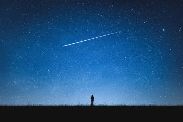 Photo of Silhouette of girl standing on mountain and night sky with shooting star. Alone concept.