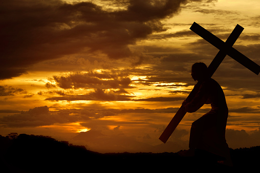 Silhouette of Jesus christ carrying cross over sunset background