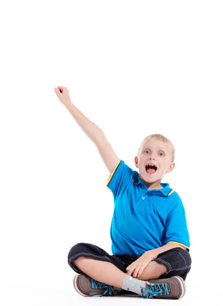 istock Excited little blond boy sitting cross-legged raises hand 1080736414