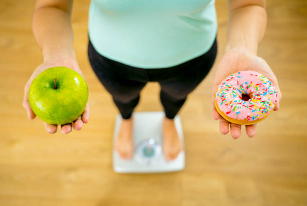 cerca de la mujer en escala sobre apple manos y dona escoger entre postre alimentos poco saludables saludables mientras que mide el peso en concepto de dieta y tentación de cuidado de salud de nutrición. - consumption scale fotografías e imágenes de stock