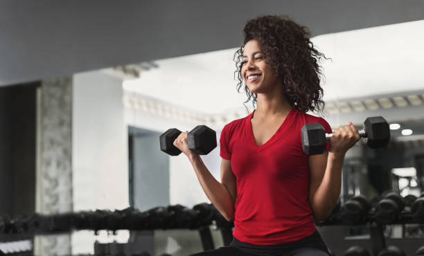 mujer afroamericana fitness haciendo ejercicios de bíceps en el gimnasio - muscular build fotografías e imágenes de stock