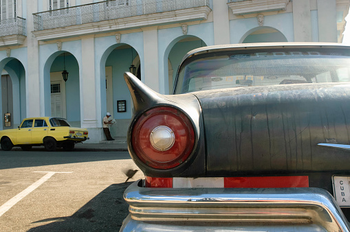 Man reading newspaper with an American Classic car and a Russian yellow Lada parked on the streets of Cienfuegos, Cuba.