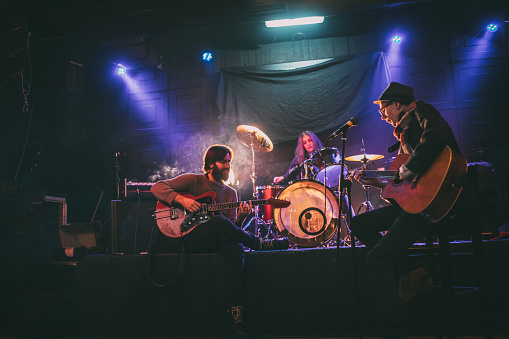 Group of people, men and woman, young band, playing music instruments indoors on stage.