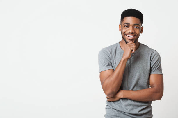 Interested smiling african-american man touching chin, copy space Interested african american man touching chin and smiling, white studio background, copy space male likeness photos stock pictures, royalty-free photos & images