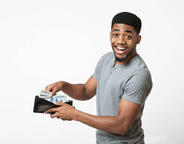 excited african-american man putting money into wallet - wallet buying white dollar imagens e fotografias de stock