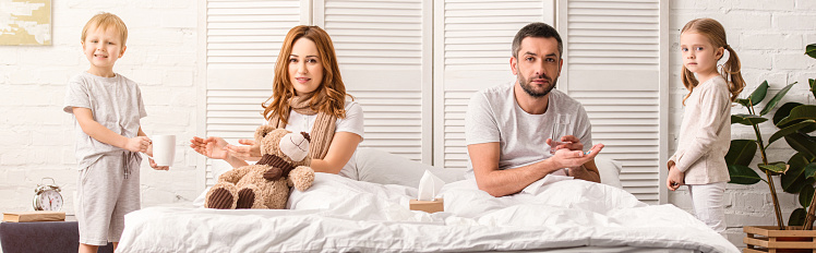 panoramic view of children supporting sick mother and father in bedroom