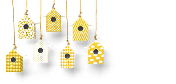 Photo of A set of painted birdhouses are suspended on a rope. Birdhouses with yellow and white patterns isolated on a white background with space for text.
