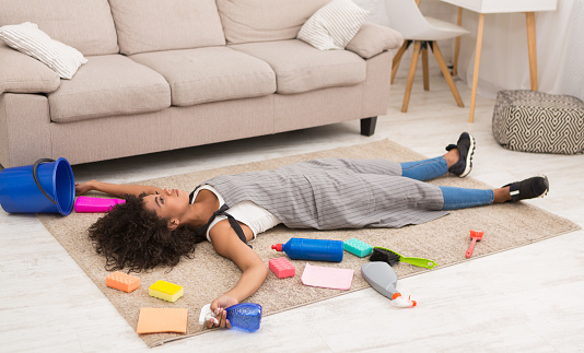 Tired african-american woman lying on floor with detergents, rest after housework at home, copy space