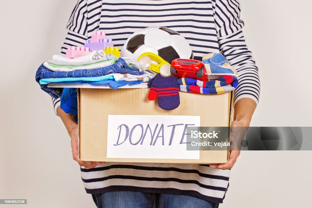 Mano de mujer caja de donación con ropa, juguetes y libros para la caridad - Foto de stock de Donación benéfica libre de derechos