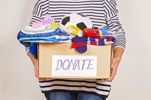 服、おもちゃや慈善事業のための本と募金箱を持つ女性の手 - carry clothes ストックフォトと画像