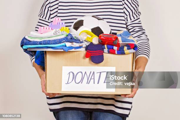 Woman Hand Holding Donation Box With Clothes Toys And Books For Charity Stock Photo - Download Image Now