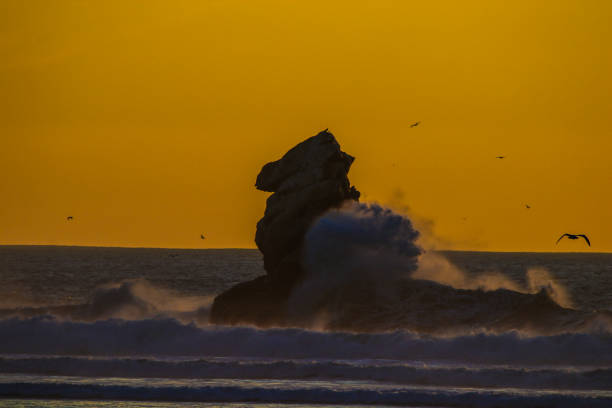The sun sets over the Pacific Ocean in Morro Bay California and past tge iconic ancient extinct volcanic plug