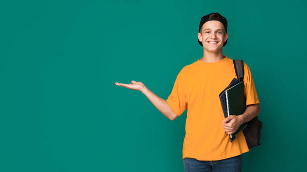 Happy student with books holding something on palm Happy student with books holding something on palm over turquoise background, copy space male likeness stock pictures, royalty-free photos & images
