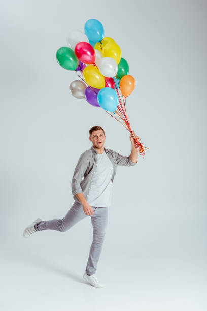 istock man jumping with bundle of colorful balloons and looking at camera on grey background 1080930734