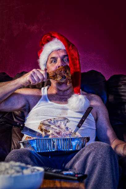 istock A man eating the last drumstick from a leftover turkey dinner from carcass in his lap wearing a Santa hat 1080937776