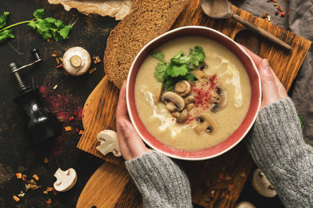 Bowl of mushroom cream soup in woman hands in a woolen sweater. Rustic dark background, top view, flat lay. Winter warming soup on vintage cutting boards. Bowl of mushroom cream soup in woman hands in a woolen sweater. Rustic dark background, top view, flat lay. Winter warming soup on vintage cutting boards winter rye stock pictures, royalty-free photos & images