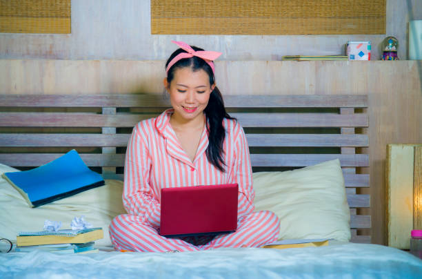 mujer de adolescente joven lindo y feliz nerd asiático chino estudiante en pelo de nerd de la cinta de estudiando en casa habitación sentado en cama con ordenador portátil y libros de texto sonriendo seguro - nerd student female exam fotografías e imágenes de stock