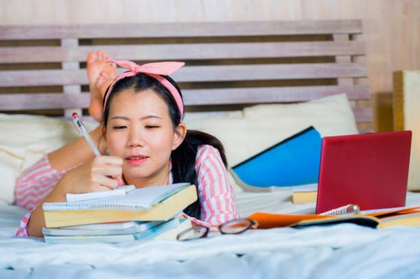 chica joven linda y feliz nerd asiático coreano estudiante adolescente pelo nerd de la cinta de estudiando en casa habitación sentado en cama con ordenador portátil y libros de texto sonriendo seguro - nerd student female exam fotografías e imágenes de stock