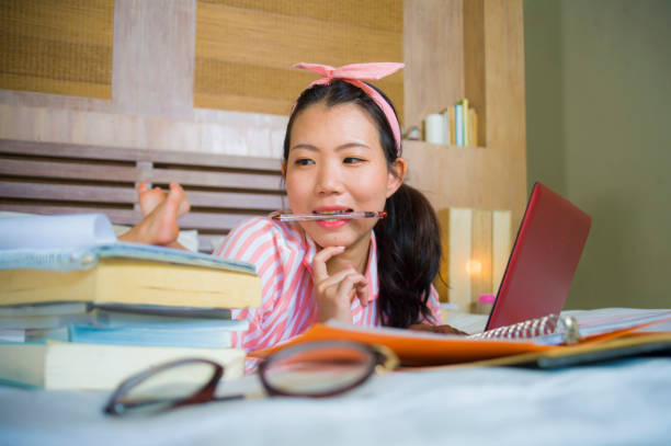 chica joven linda y feliz nerd asiático chino estudiante adolescente pelo nerd de la cinta de estudiando en casa habitación sentado en cama con ordenador portátil y libros de texto sonriendo seguro - nerd student female exam fotografías e imágenes de stock