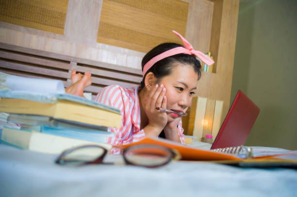 chica joven linda y feliz nerd asiático coreano estudiante adolescente pelo nerd de la cinta de estudiando en casa habitación sentado en cama con ordenador portátil y libros de texto sonriendo seguro - nerd student female exam fotografías e imágenes de stock