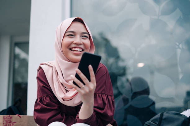 若いアジアのイスラム教徒の女性のスマート フォンを再生 - malaysia ストックフォトと画像