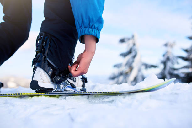 Snowboarder straps in his legs in snowboard boots in modern fast flow bindings with straps. Rider at ski resort prepares for freeride session. Man wearing fashionable outfit. stock photo