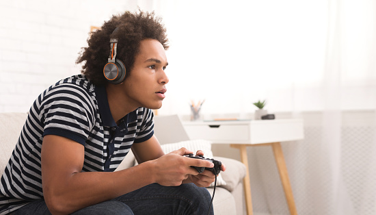 Concentrated teenager playing video games with joystick at home, copy space