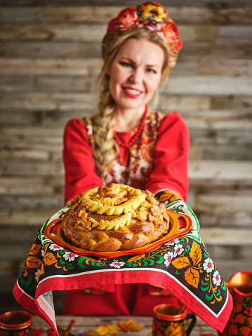 A Russian woman holding a traditional Russian karavai holiday bread on a table.