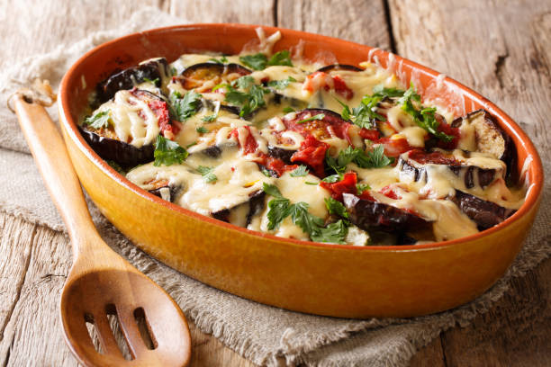 healthy meal of baked eggplants with tomatoes, herbs and cheese close-up in a baking dish. horizontal stock photo