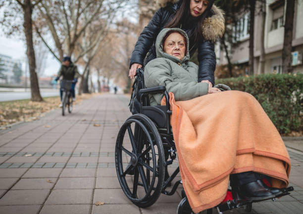 senior woman in a wheelchair with a helping hand - senior adult wheelchair community family imagens e fotografias de stock