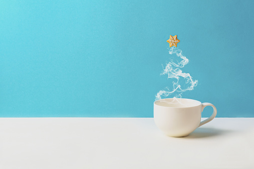 Cup of tea or coffee with steam in fir tree shape with gingerbread cookies on blue background. Christmas celebration concept. Copy space. Toned