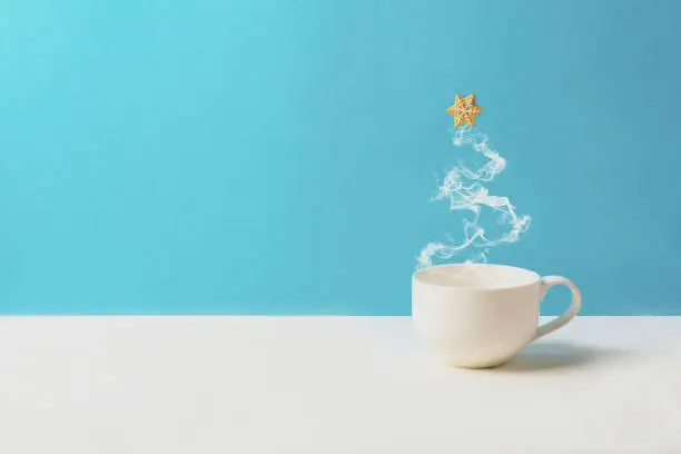 Photo of Cup of tea or coffee with steam in fir tree shape with gingerbread cookies on blue background. Christmas celebration concept. Copy space. Toned