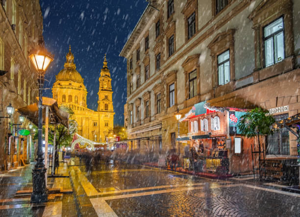 Budapest, Hungary - Snowy night at a Christmas market and shopping street with street-lamp, festive decoration and St.Stephen's basilica at background stock photo