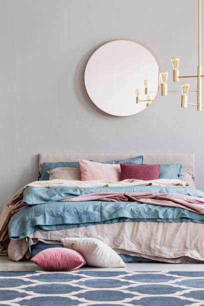 istock Chick round mirror on grey empty copy space wall in elegant bedroom interior with warm bed with blue, pastel pink and beige bedding 1081020410