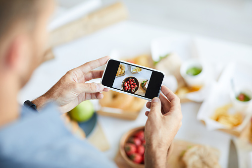 Close up of unrecognizable man taking pictures of food using smartphone, copy space