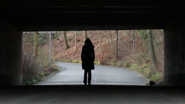 Silhouette of Woman walking under a bridge in 4K. Lonely melancholic sad atmosphere concept of destiny journey road direction