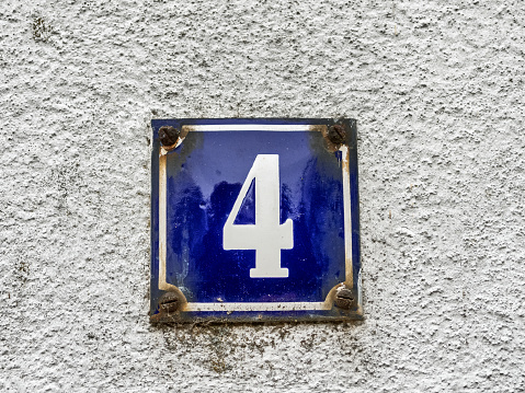 Wall of an old house in a little Bavarian town. House number 4. An old-fashioned rusty enamel sign. White number on dark blue background.