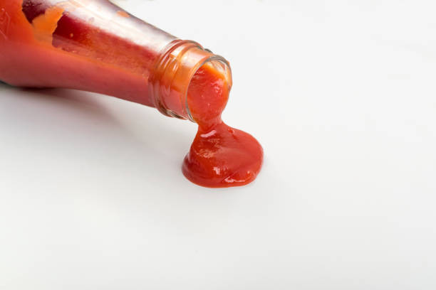 Tomato sauce is poured from the glass bottle on white background. Red puddle of tomato dressing or ketchup spot