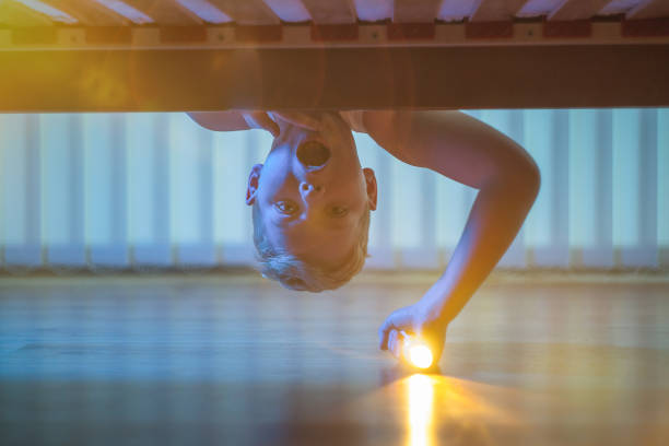 the boy with a flashlight look under bed. night time - happy kid flash imagens e fotografias de stock